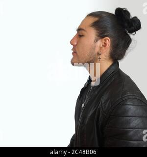 Young hispanic man with gathered hair done bow in black dress and black leather jacket, seen in profile on white background Stock Photo