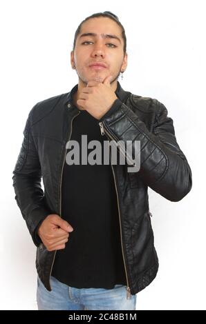 Young hispanic man with gathered hair done bow in black t-shirt and black leather jacket, with one hand on his jaw and thoughtful attitude, with the l Stock Photo