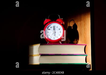 Closeup of red clock on the books illuminated by the rising sun Stock Photo