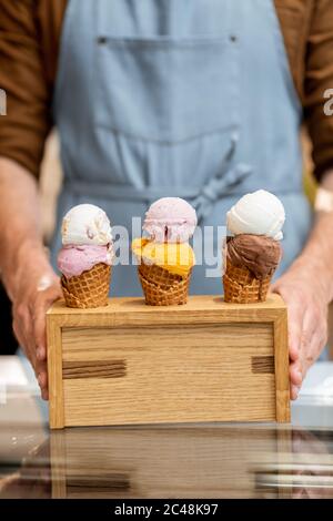 Seller putting a stand with three yummy ice creams in waffle cones with different flavor on the counter of a shop, close-up Stock Photo