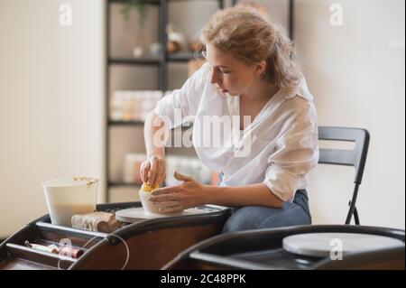 Woman working on potters wheel making dishes with their own hands. Close-up photo of dirty hands molding clay Stock Photo