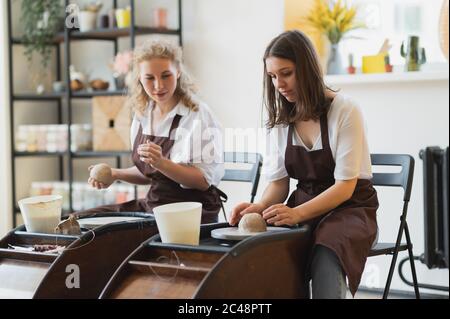 Two girls working on potters wheel making clay handmade craft in pottery workshop, friendship and guidance concept Stock Photo