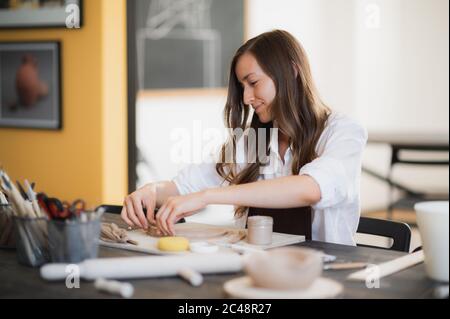 Close up of skilled craftswoman removing part of clay while making ceramic product in pottery workshop Stock Photo