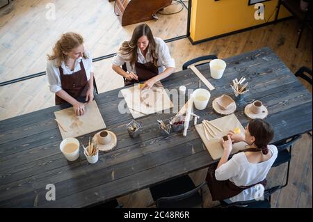 In the clay workshop. Female potters talking and smiling during the working process in the clay workshop. Female potter masters rolling up the clay on Stock Photo