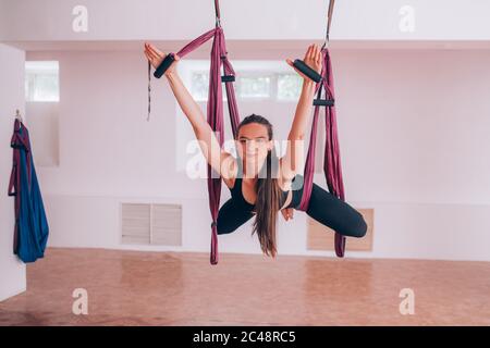 Beautiful young girl practices fly yoga on a hammock, stretching back and legs, taking care of health Stock Photo