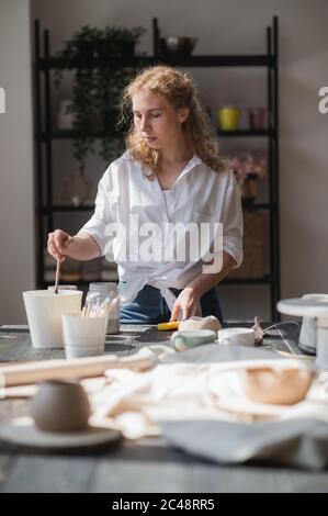 Female potter making ceramic dishes at her studio. Working process of glazing ceramic bowl. Stock Photo