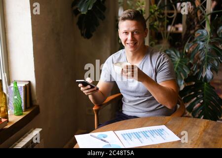 European smiling freelancer working with docments and smartphone at cafe. Stock Photo