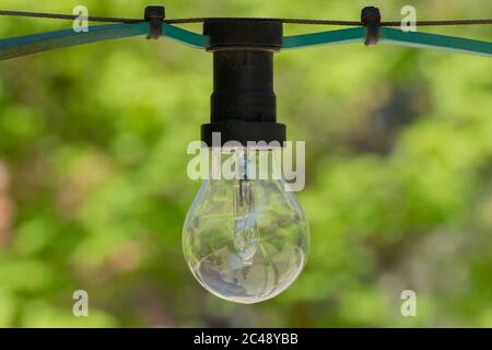 Close up of a dirty old light bulb hanging on a light chain in a park, bokeh Stock Photo