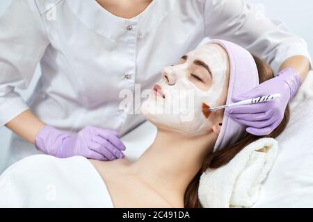 beautician applies the mask to the face of beautiful young woman at wellness spa. spa treatments Stock Photo