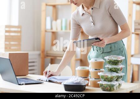 Close-up of young woman using digital tablet and making notes in note pad she working in food delivery service Stock Photo