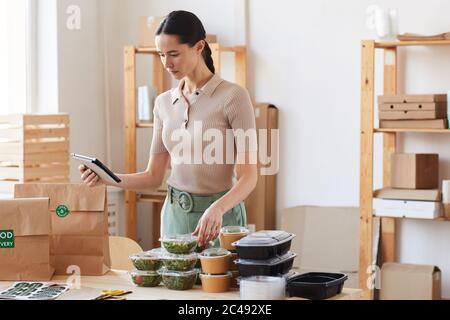 Young woman using tablet pc and checking the food while working in food delivery service Stock Photo