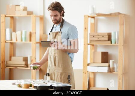 Young man in apron using tablet pc and making delivery of healthy food at office Stock Photo