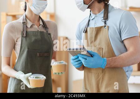 Close-up of two people in protective masks and gloves using tablet pc in work they making food delivery Stock Photo