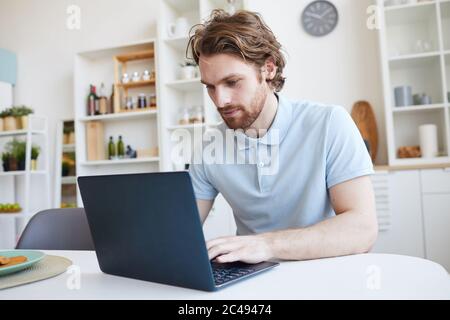Young man sitting at the table and using laptop computer at home Stock Photo