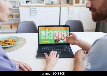 Close-up of young man pointing at monitor of laptop and suggesting to woman to order food online Stock Photo
