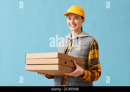 Portrait of young woman in uniform smiling at camera and delivering pizza she standing against the blue background Stock Photo