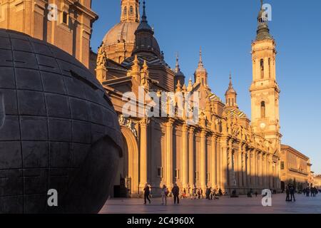 Wide-angle view of the Cathedral of Our Lady of the Pillar on square of the same name in Zaragoza, Spain. People walking at golden hour before sunset. Stock Photo