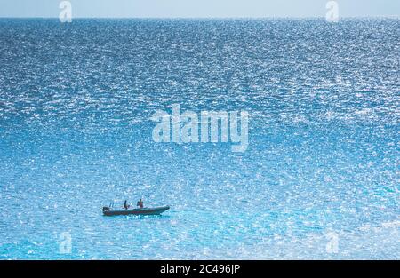 Distant motor boat with two people in it on the sparkling surface of the sea. Aerial view. Stock Photo