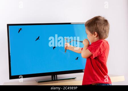 Cute small boy aiming to a TV screen with a slingshot. The targets