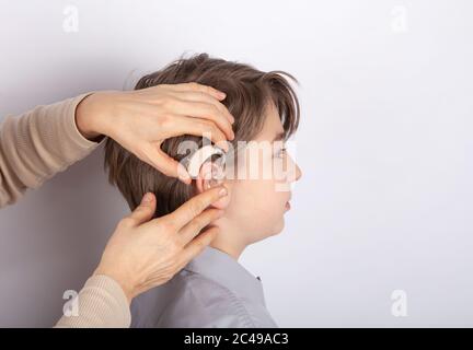 Close up of doctor's hands inserting hearing aid in a youg boy patient's ear Stock Photo