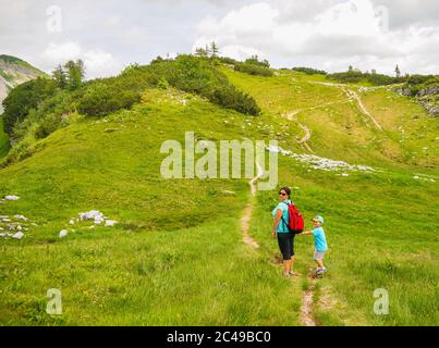 AUSSEERLAND, AUSTRIA - Jul 22, 2019: Woman with backpack and child walking on a small footpath on a mountain Stock Photo