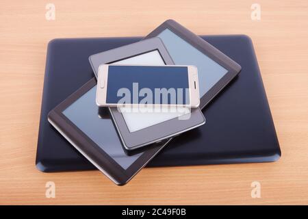 Stack of different gadgets like smartphone, ebook reader, tablet device and a notebook on a wooden table. Stock Photo