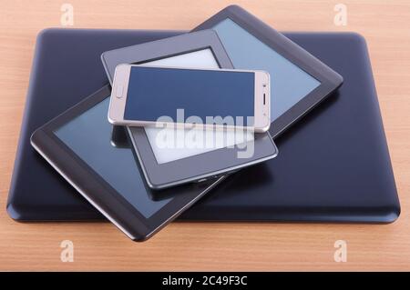 Stack made of different gadgets: from smartphone, ebook reader, tablet device and a notebook on a wooden table. Stock Photo