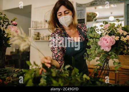 European female florist with a medical face mask making flower ...