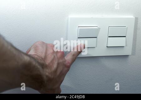 A finger turning on lighting switch on rough on white dark wall. Stock Photo