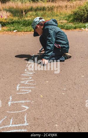 POZNAN, POLAND - May 30, 2020: Six year old Polish Caucasian boy writing with crayon on a footpath in the Jan Pawla park Stock Photo