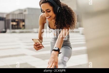 Fitness woman using an app on her phone while exercising. Smiling woman doing stretching workout and using smart phone.