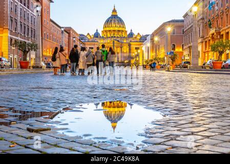 Vatican City by night. Illuminated dome of St Peters Basilica and St Peters Square. Group of tourists on Via della Conciliazione. Rome, Italy.