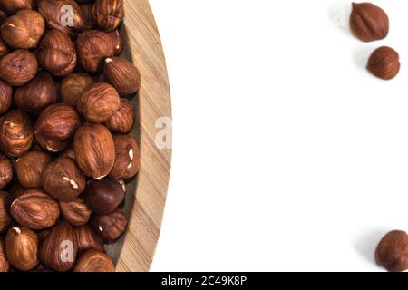 Hazelnuts in a bowl to the left and three hazelnuts outside on a white background Stock Photo