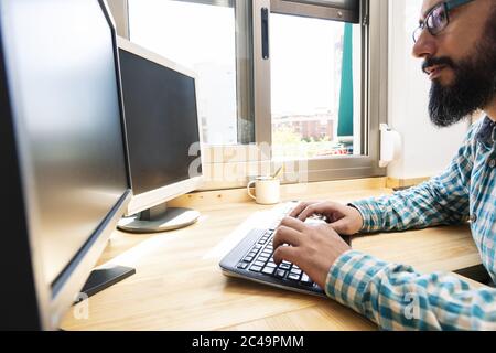 man typing on a keyboard in front of two computer screens, work from home concept Stock Photo