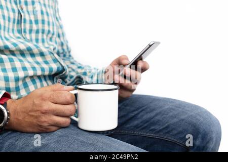 close-up of the hands of a man with a cup of coffee while consulting the phone, communication concept and technology Stock Photo