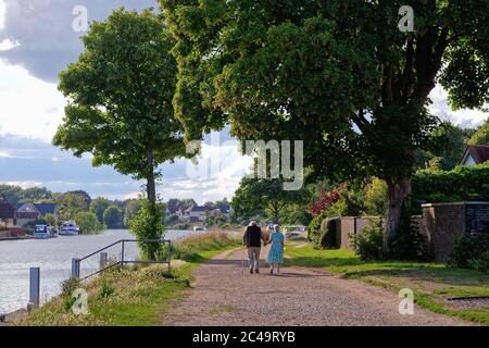 Rear view of an old couple holding hands while strolling on the footpath by the River Thames at Laleham on a summers evening Surrey England UK Stock Photo