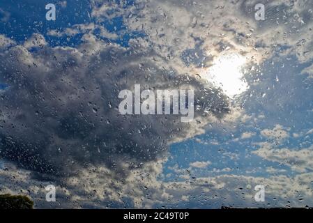 Close up of raindrops on a window against a background of the sun, rain clouds and blue sky Stock Photo
