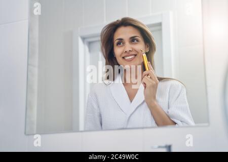 Joyful young woman using golden facial massager in bathroom Stock Photo