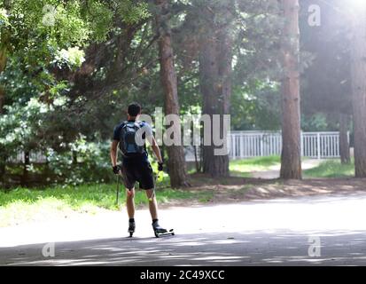 Man is cross-country skiing with roller ski in the park. Sport roller skiing. Stock Photo
