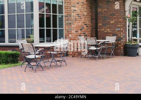 Empty patio in summer in recreation in the town. White wooden table and armchairs on outdoor terrace of summer cafe. Restaurant business awaits visito Stock Photo