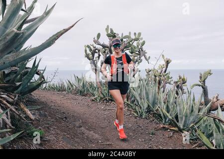 Woman runs cross country on a path in mountain path at Canary Island. Ocean view Stock Photo