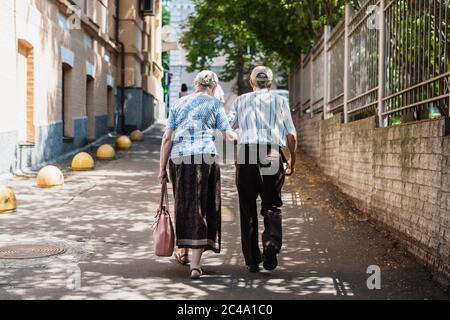 Senior couple walking arm in arm along the street. Back view. Concept of supporting each other in old age