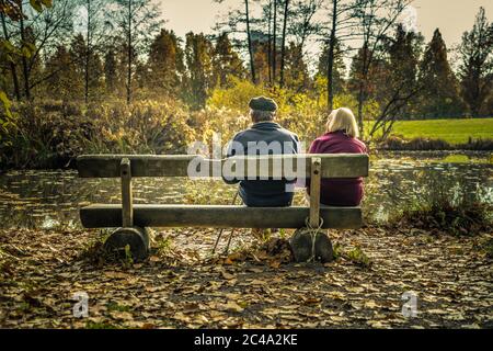 An old couple sits in a park and enjoying the sun together. The photo is about staying together and preserve the love for a lifetime. Stock Photo