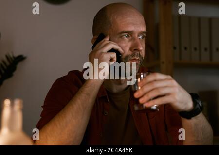 Mature man talking on his mobile phone and holding glass with alcohol Stock Photo