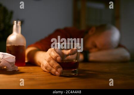 Image of glass with alcohol on the table with drunk man sleeping in the background Stock Photo