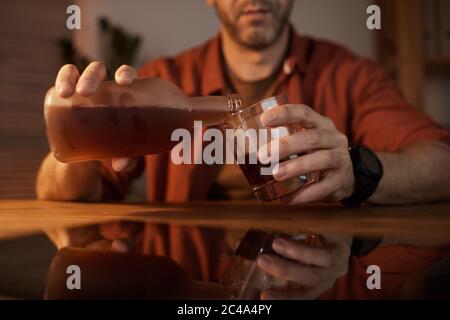 Close-up of young man sitting at the table and pouring alcohol from the bottle into the glass Stock Photo