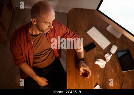 High angle view of mature man drinking alcohol after hard working day he sitting at his workplace in front of computer Stock Photo