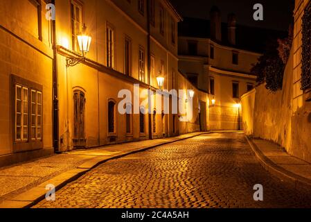 Narrow cobbled street in old medieval town with illuminated houses by vintage street lamps, Novy svet, Prague, Czech Republic. Night shot. Stock Photo