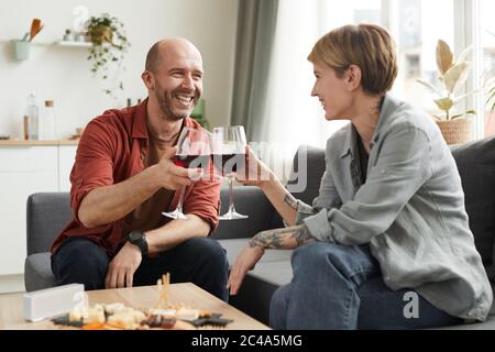 Mature man smiling to woman while they sitting on the sofa and drinking wine from wineglasses Stock Photo