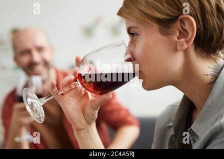 Close-up of young woman drinking red wine from the wineglass with man sitting in the background Stock Photo